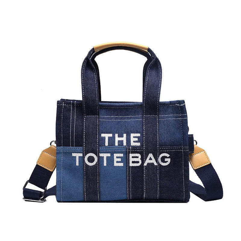 A dark blue canvas tote bag with tan leather handles and trim, featuring white text that reads THE TOTE BAG.