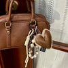 Brown leather handbag with a heart pendant keychain featuring long natural fiber tassels