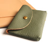 A folded olive green genuine leather card holder and coin purse resting on a light tan leather wallet.