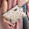 A hand holds a beige cartoon cat cosmetic pouch with various cat illustrations against a pink cardigan.