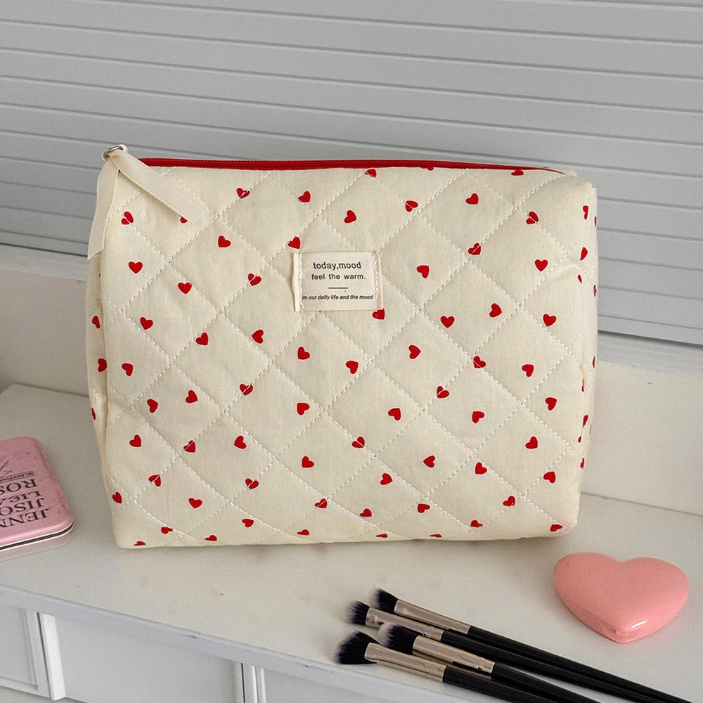 A cream-colored quilted makeup bag with a red lining and small red hearts, resting on a white surface.
