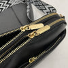 A close-up view of a black vegan PU crossbody bag with gold zippers and a patterned strap.