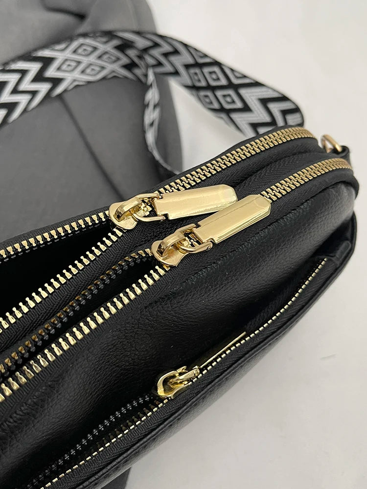 A close-up view of a black vegan PU crossbody bag with gold zippers and a patterned strap.