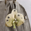 A realistic pale green orchid flower keychain attached to a gray fabric strap.
