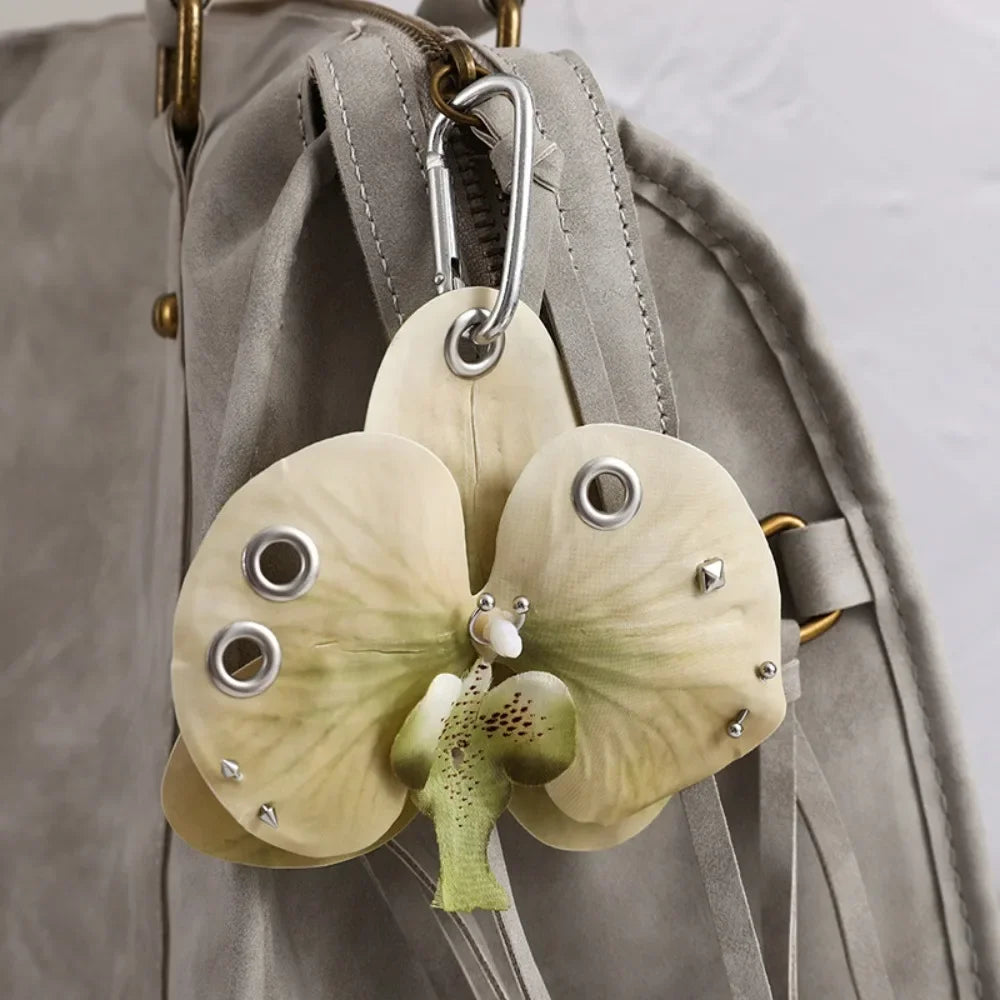 A realistic pale green orchid flower keychain attached to a gray fabric strap.