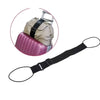 Una correa de equipaje negra ajustable junto a una mochila beige y un objeto cilíndrico rosa.