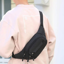 A person is wearing a black adjustable waist bag with a 4-zip belt on a light pink jacket.