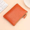 An orange genuine leather mini zipper coin and card purse resting on a light background next to a white keyboard.