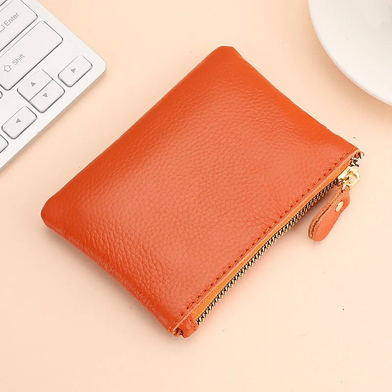 An orange genuine leather mini zipper coin and card purse resting on a light background next to a white keyboard.