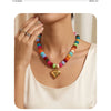 A woman is wearing a colorful bead necklace with heart-shaped charms and resin accents against a light background.