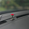 Eine kleine rote Rosenblume liegt auf einer schwarzen Kunststoffoberfläche im Autointerieur.