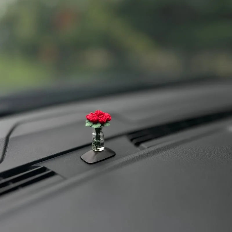 Eine kleine rote Rosenblume liegt auf einer schwarzen Kunststoffoberfläche im Autointerieur.