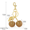 Gold-colored crystal cherry fruit keychain with a loop and hanging fruit.