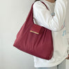 A person holds a maroon reusable nylon mini keychain tote bag with a gold accent against a white sweatshirt.