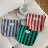Tres fundas de almacenamiento de lienzo en colores rayados rosa, marrón y verde sobre una superficie blanca con una taza de c