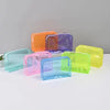 A collection of transparent PVC travel makeup bags in various colors including orange, purple, pink, blue, and lime green.