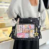 A black transparent shoulder tote bag decorated with stickers and charms is held by a person in a light gray sweater.