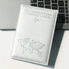 A white leather passport holder with a silver embossed world map and an airplane icon resting on a gray laptop.