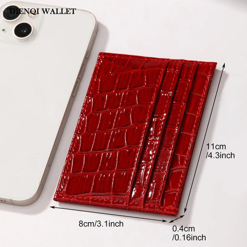 A red crocodile pattern slim card holder wallet next to a white smartphone.