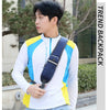 A young man wearing a white long-sleeved shirt with blue and yellow accents, carrying a navy nylon chest sling bag.
