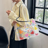 A person holds a clear plastic shoulder bag with yellow and pink floral patterns next to a window.