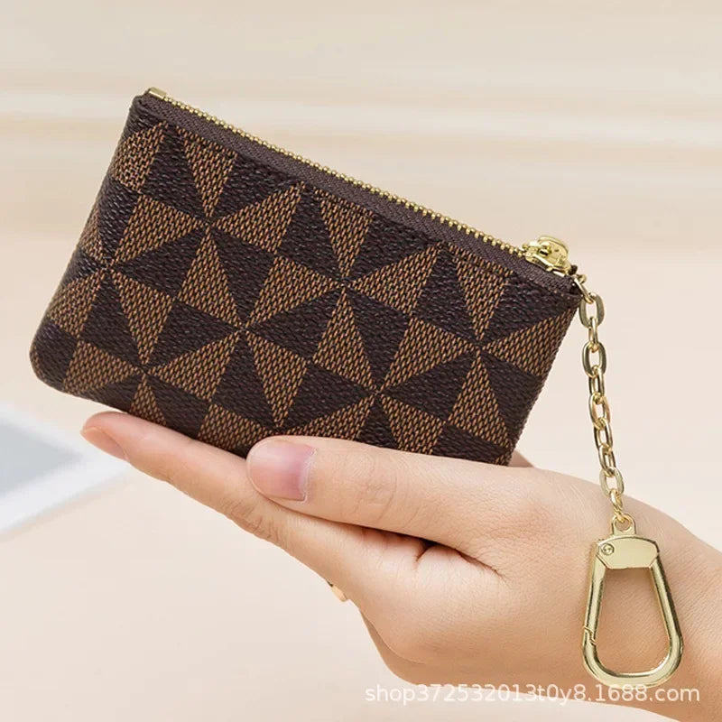 A brown geometric mini coin purse with a gold chain is held in a person's hand.