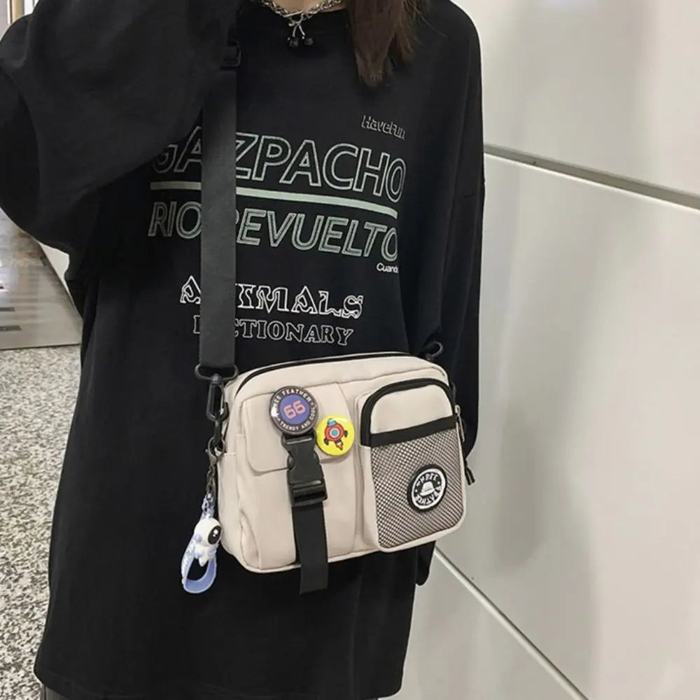 A woman holds a beige canvas shoulder bag with black straps and yellow accents against a black shirt.