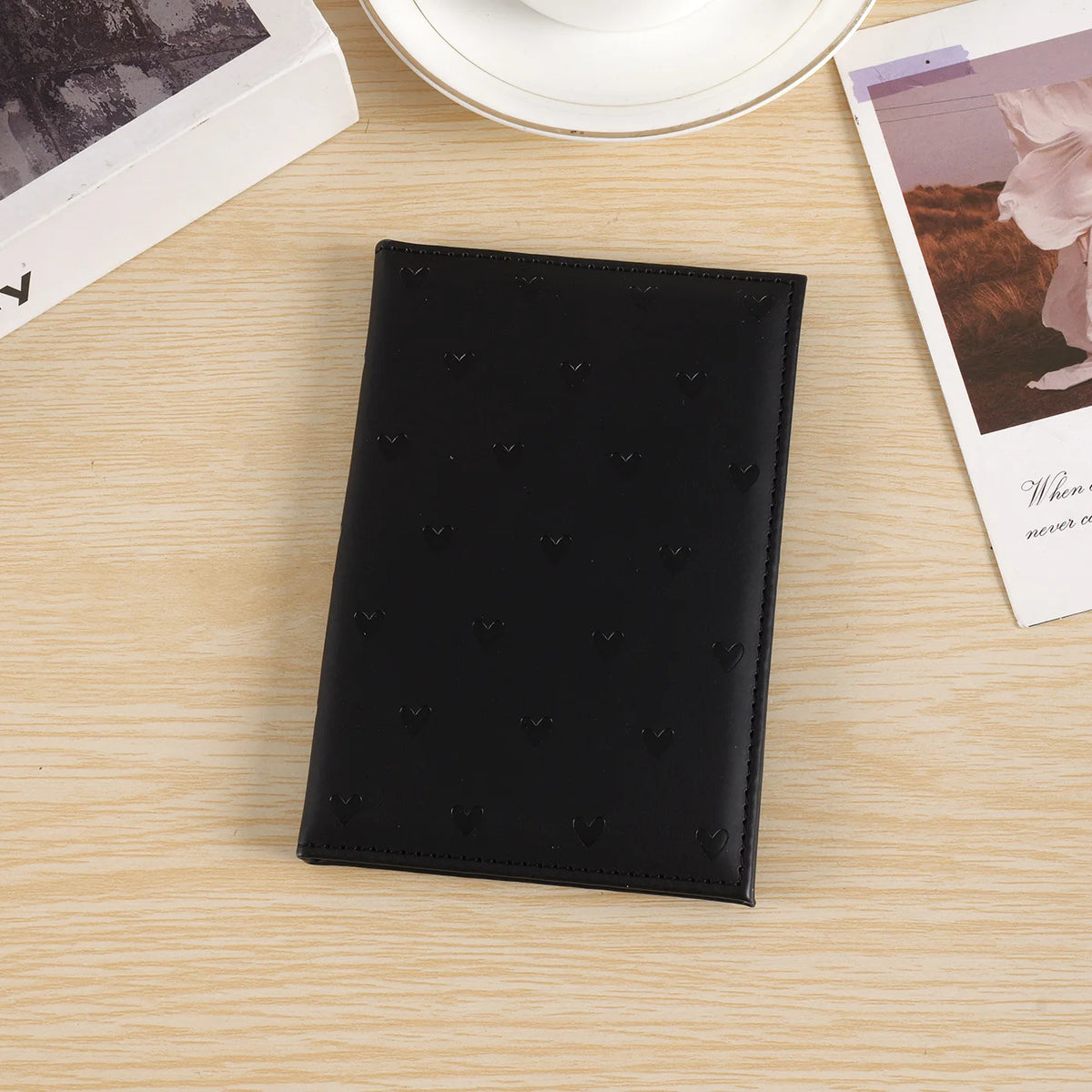 Black leather heart print passport cover travel wallet resting on a light wooden surface.