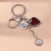 Silver keychain featuring a heart pendant, an eye pendant, and a sun pendant.