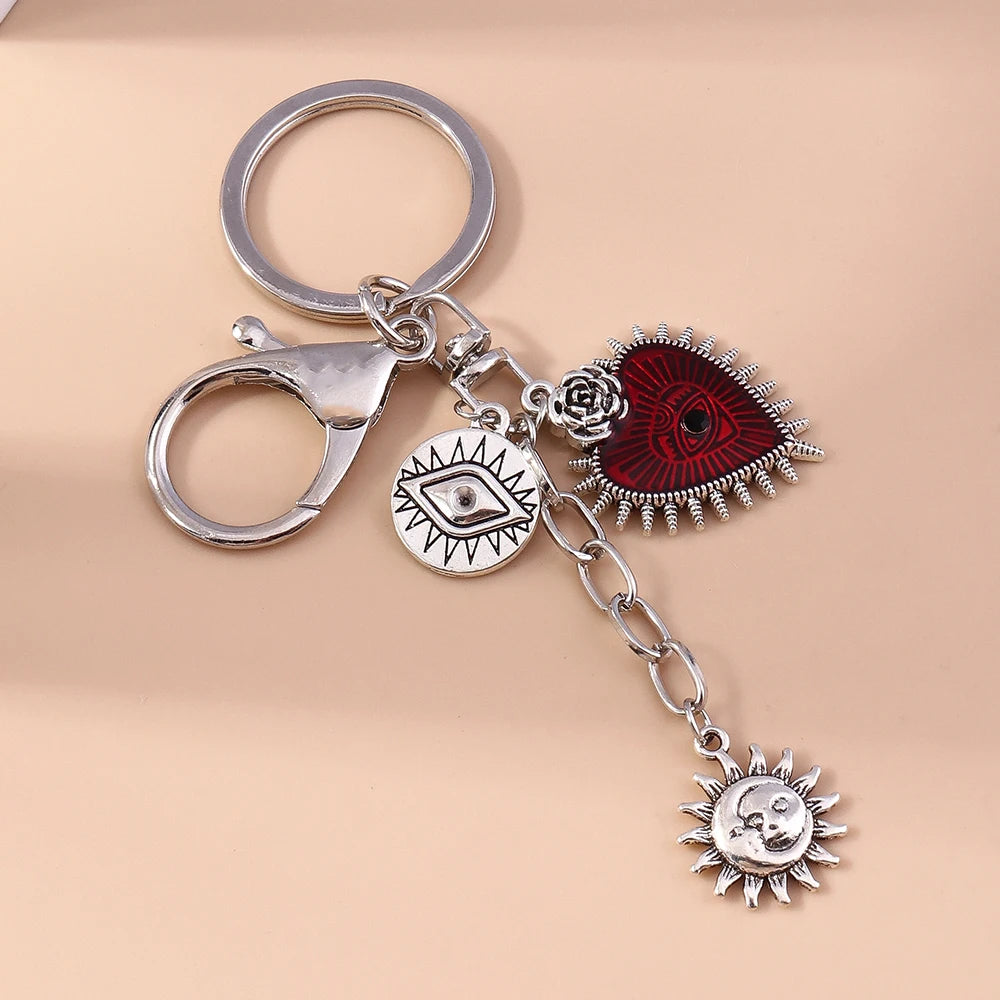 Silver keychain featuring a heart pendant, an eye pendant, and a sun pendant.