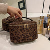 A brown leopard print faux suede cosmetic bag is displayed on a white surface next to various glass bottles.