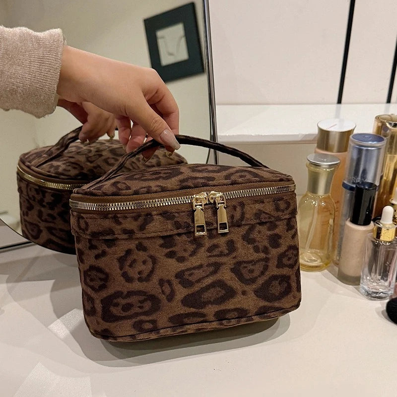A brown leopard print faux suede cosmetic bag is displayed on a white surface next to various glass bottles.