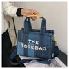 A dark blue denim tote bag with white stitching and a light blue accent, held by a hand.