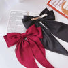 A dark red silk bow hair clip with a gold-toned bar is displayed next to a book.