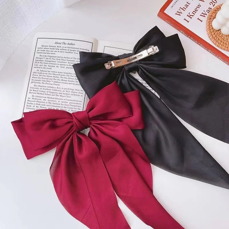 A dark red silk bow hair clip with a gold-toned bar is displayed next to a book.