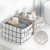 A white storage basket with a black grid pattern holds various bathroom or desk items like soap and lotion bottles.