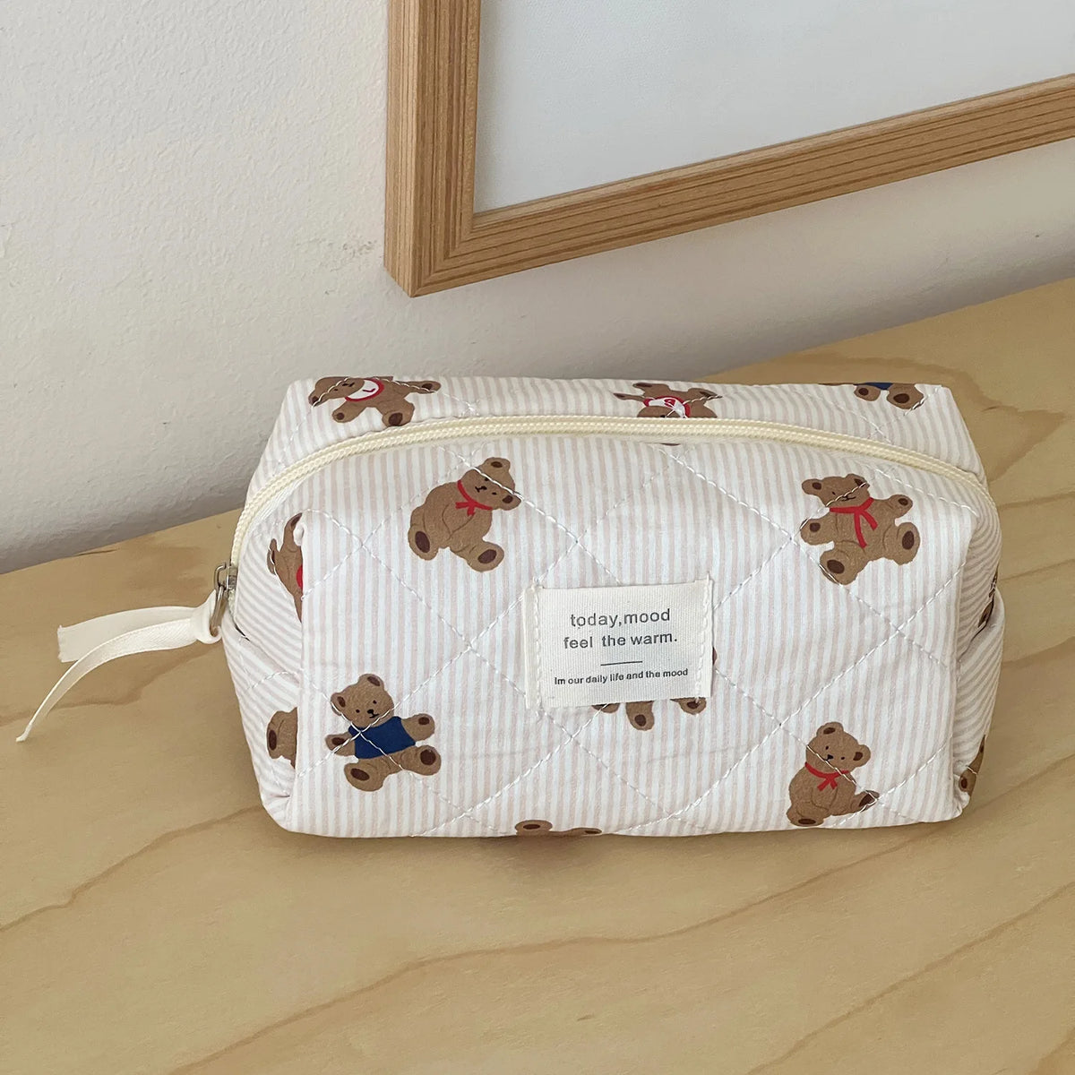 A quilted striped cosmetic makeup bag featuring small bear embroidery, resting on a light wooden surface.
