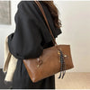 A woman holds a brown leather tote bag with a gold-toned strap and a textured fabric in a black coat.