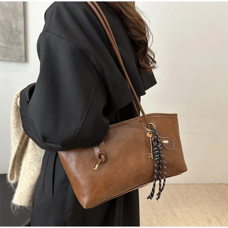 A woman holds a brown leather tote bag with a gold-toned strap and a textured fabric in a black coat.