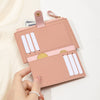 A pink card holder wallet with white cards and gold accents is held by a hand.