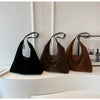 A set of three suede slouchy shoulder bags in black, brown, and tan displayed against a white wall.