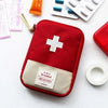 A red pouch containing a white cross first aid kit and pills, resting on a white surface.
