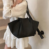 A woman holds a black luxury PU leather shoulder tote bag against a white dress.