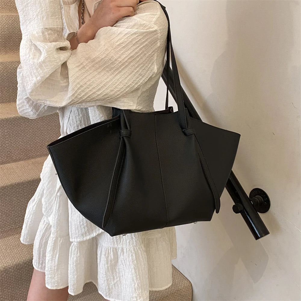 A woman holds a black luxury PU leather shoulder tote bag against a white dress.