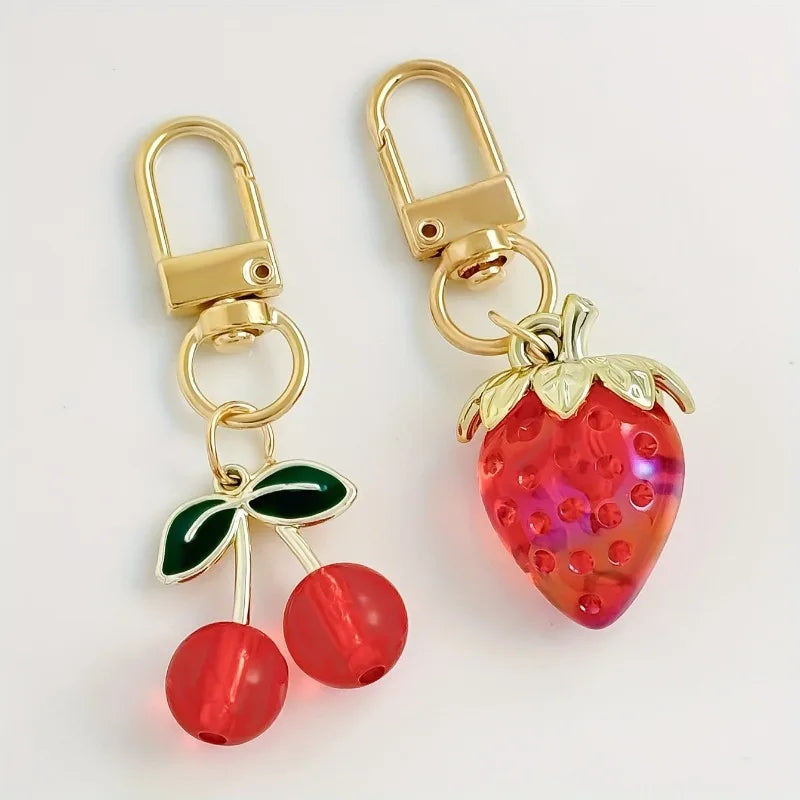 A set of gold-toned fruit keychains featuring a strawberry and cherry bag charms.