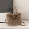 A fluffy taupe faux fur tote bag with a tan leather crossbody strap resting on a white surface.