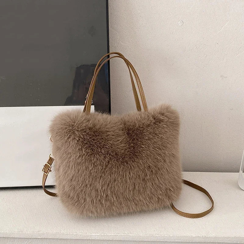 A fluffy taupe faux fur tote bag with a tan leather crossbody strap resting on a white surface.