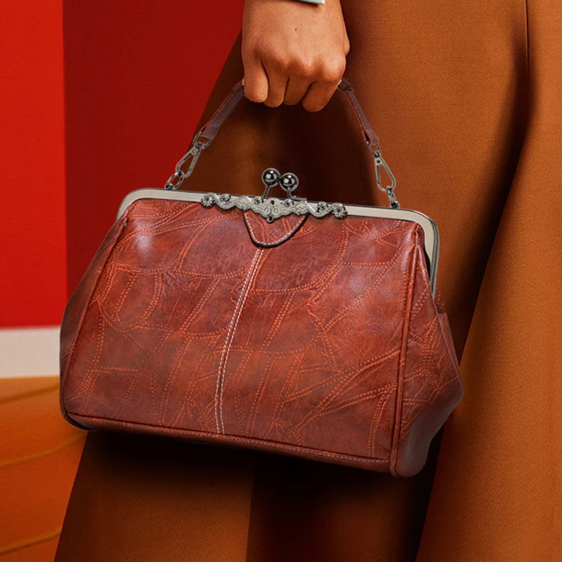 A brown leather crossbody bag with silver hardware is held by a person against a red background.