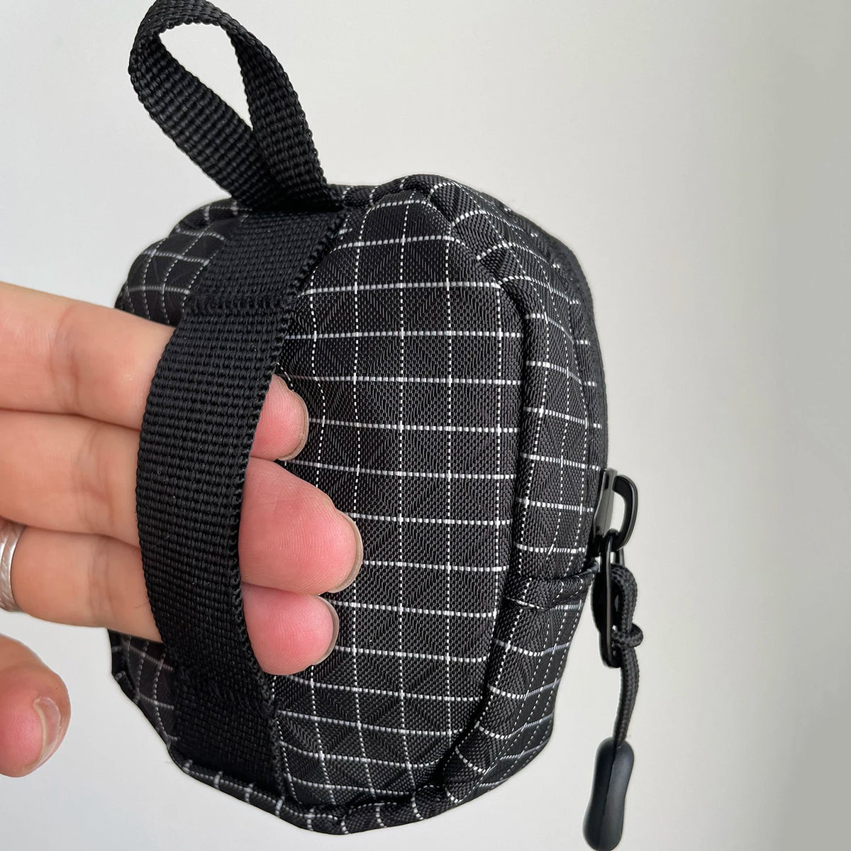 Une main tient une pochette utilitaire à carreaux noirs pour clés et essentiels.