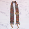 A close-up of a retro textile replacement bag strap featuring intricate geometric patterns in orange, blue, and brown on a wh
